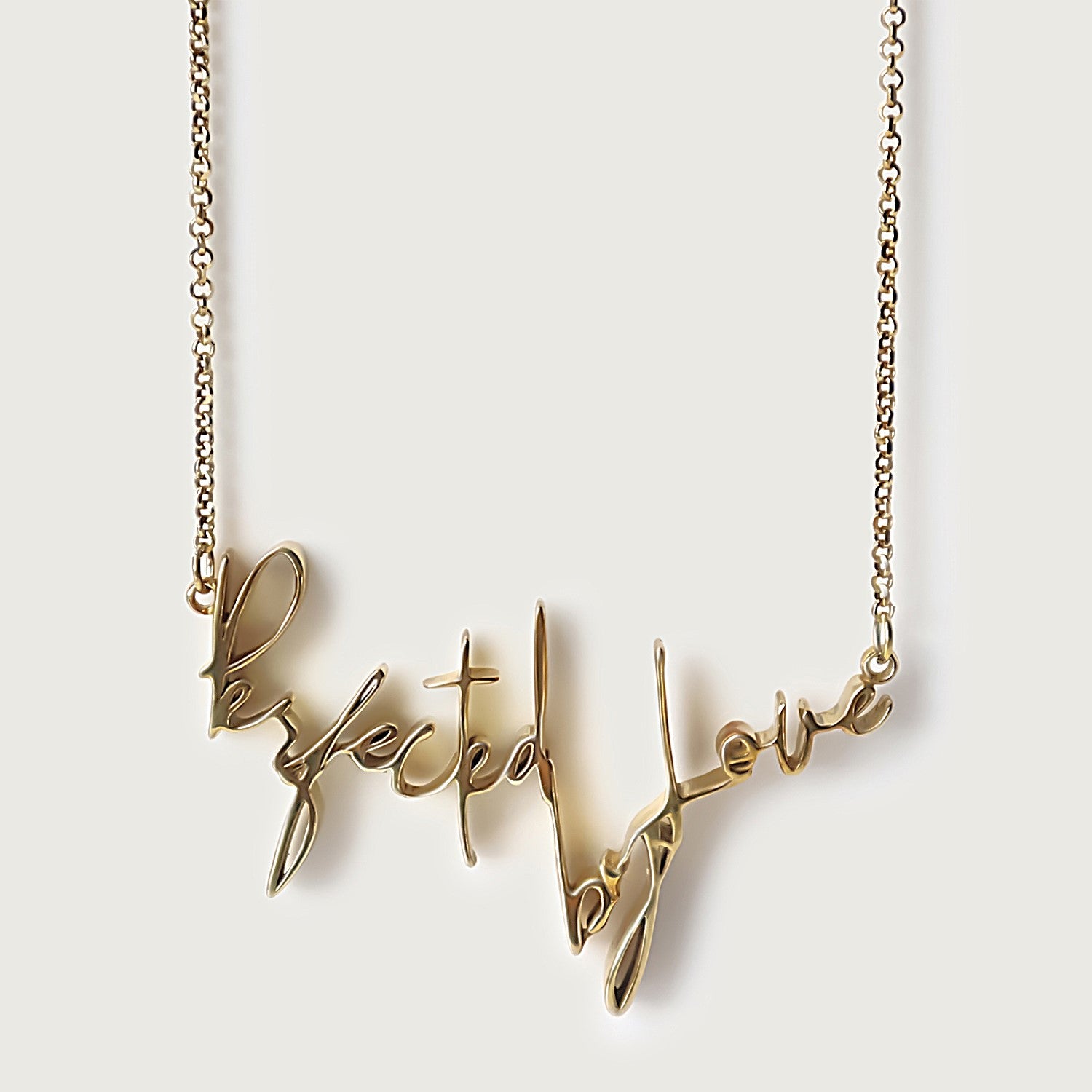 An 18K gold vermeil necklace with a cursive script pendant that reads 'Perfected by Love'.